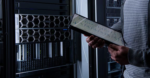 A technician holding a server component in front of equipment racks.