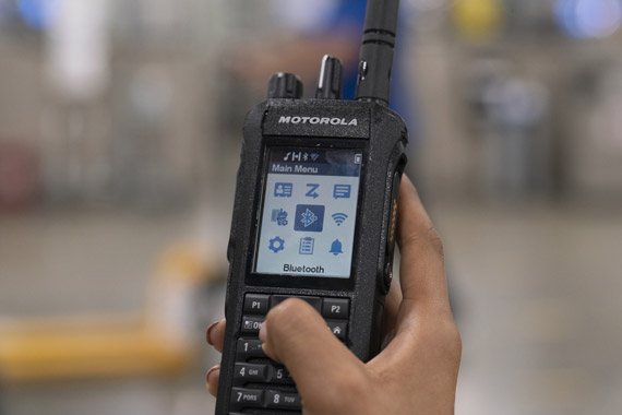 A hand holding a two way radio, its menu open on the screen.